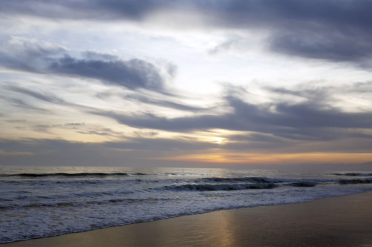 Ocean view of small waves with the setting sun behind clouds reflecting off the Pacific Ocean. Hollywood Beach, Channel Islands California.